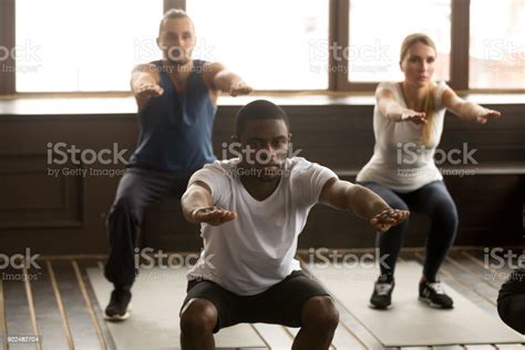 Young Africanamerican Man Doing Squat Exercises At Group Fitness