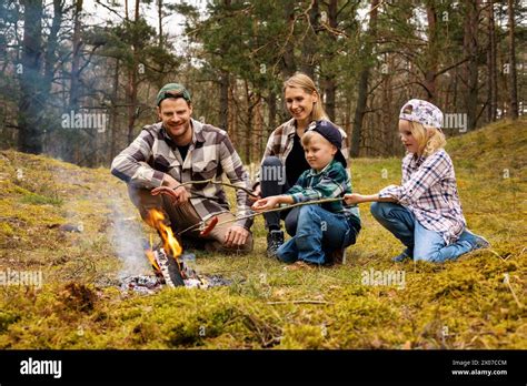 family with two children frying sausages over a bonfire while camping