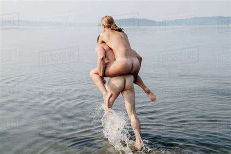 Nude Man Giving Nude Woman Piggyback Into Water Stock