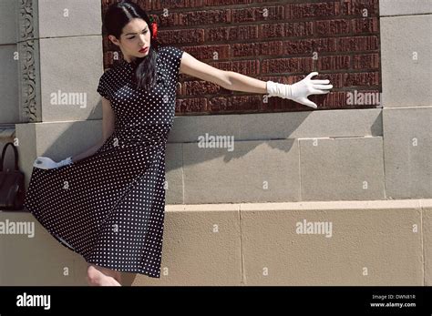 A Female Model Lean Against A Wall Wearing A Vintage Inspired Polka Dot Dress And White Glove