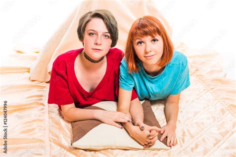 two lesbian girls lying on the blanket cover and hold hands on white isolated background