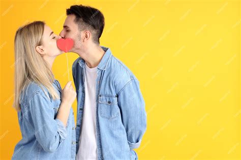 Premium Photo Cute Couple Kissing And Hide Behind A Heart On Yellow