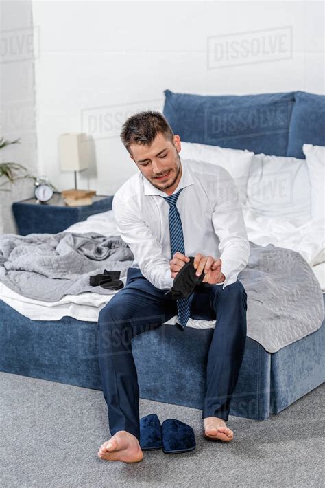 Handsome Man Sitting On Bed And Wearing Socks In Morning In Bedroom