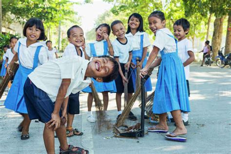 Young School Children Playing And Cleaning The Street Of Their School