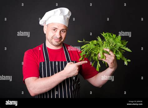 Closeup Of Happy Chef Holding Arugula Beam On Black Background Stock