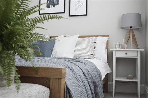 A Bed With White Sheets And Pillows Next To A Green Plant In A Room