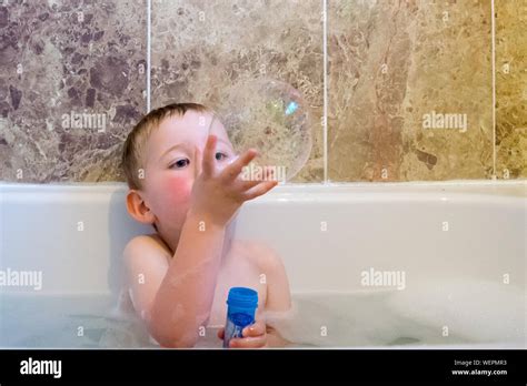 verspielte junge holding seifenblase beim sitzen in der badewanne