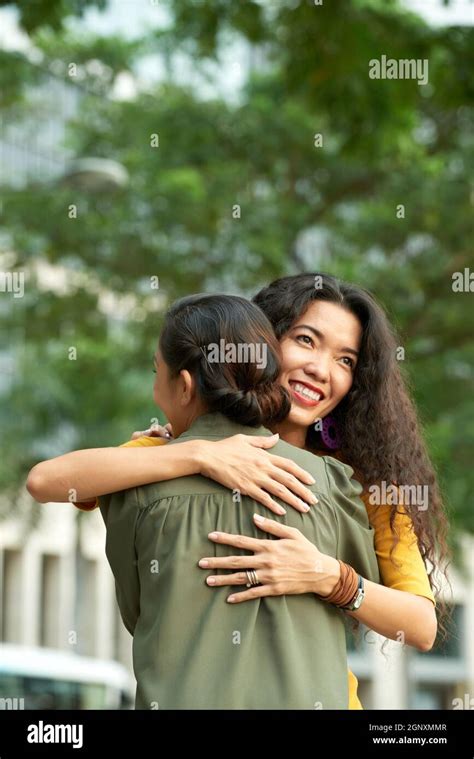 Smiling Adult Asian Daughter With Curly Hair Hugging Mother In Summer