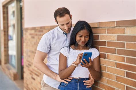 Man And Woman Interracial Couple Hugging Each Other Using Smartphone At Street Stock Image