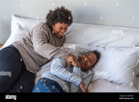 Mother Tickling Son Lying On Bed At Home Stock Photo Alamy