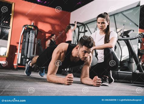 Attractive Trainer Supervising Sportsman Doing Plank Stock Photo
