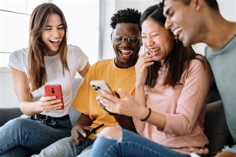 Young Group Of Diverse Friends Sitting On Sofa Using Mobile Phone Stock