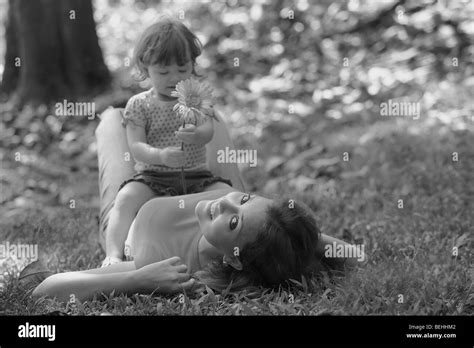 Portrait Of A Young Woman Lying On Grass With Her Daughter Sitting On