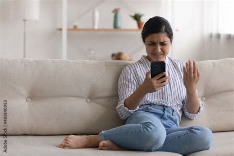 Confused Angry Indian Woman Sit On Couch At Home Read Spam Message On Phone Screen Have Problem