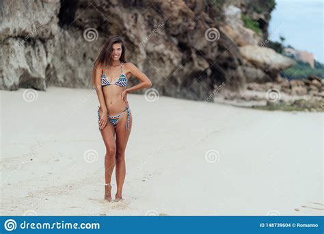 Beautiful Tanned Woman In Colored Swimsuit Rests On White Sand Beach