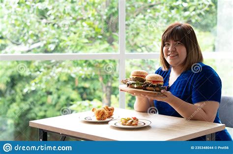 hungry overweight woman holding hamburger on a wooden plate fried chicken and pizza on table
