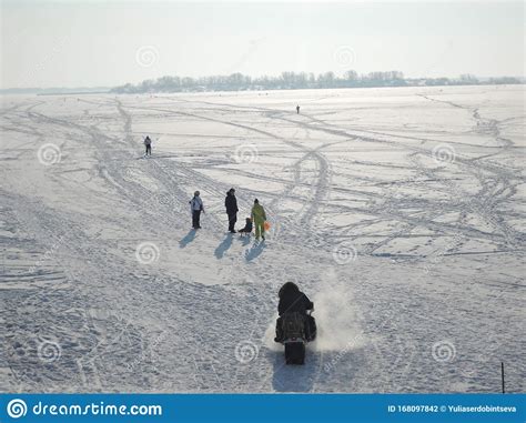 People Walk On The Frozen River Sledding Skiing And Snowmobiling