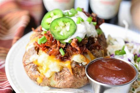 Pulled Pork Loaded Baked Potatoes On A White Plate With Sourcream And