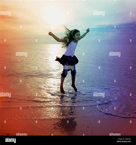 Little Girl Jumping Up And Down In The Water On The Beach Stock Photo