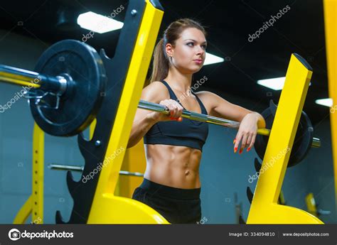Fitness Girl Posing Near The Barbell In A Modern Gym Muscles Woman