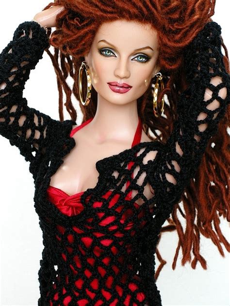 A Doll With Red Hair Wearing A Black Crochet Dress And Gold Hoop Earrings