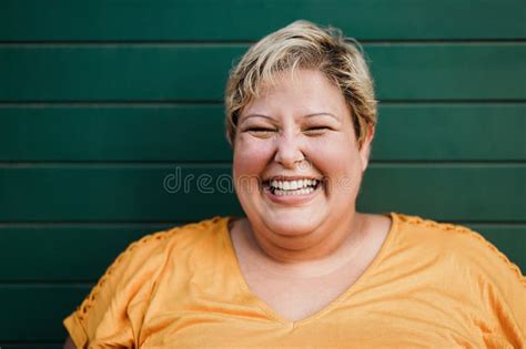 portrait of curvy woman smiling on camera outdoors with green background focus on face stock
