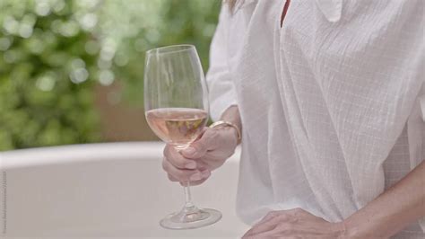 woman holding a glass of rosé wine sitting on edge of bathtub del colaborador de stocksy
