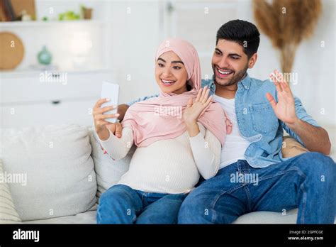 loving pregnant arab couple having video call waving hands to smartphone camera and smiling