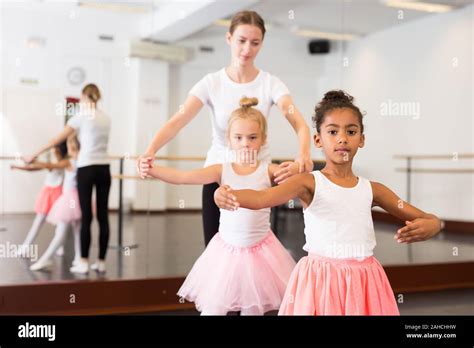 Young Female Classical Dance Teacher Helping Her Little Girls Students