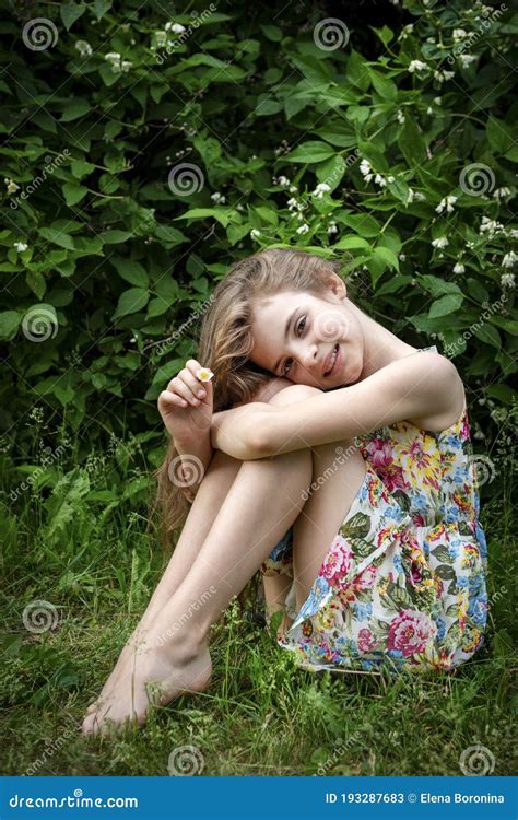 Teenage Girl With Long Hair And A Dress Is Sitting On The Grass
