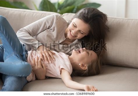 Overjoyed Mother Embrace Little Daughter Laughing Lying Together On Sofa In Living Room Joyful