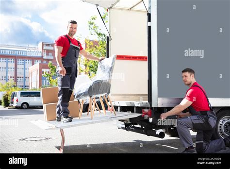 Two Young Male Movers Loading The Cardboard Boxes And Furniture In