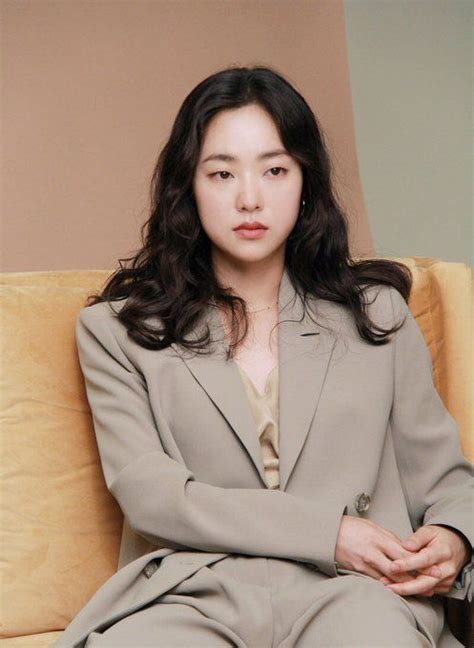 A Woman Sitting On Top Of A Couch Wearing A Gray Suit And Tan Shirt With Her Arms Crossed