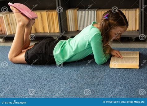 Schoolgirl Lying On Floor And Reading A Book In Library Stock Photo