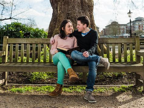Couple In Love Hugging And Dating Sitting On A Bench In A Park Stock