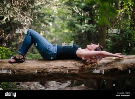 Woman Lying On Her Back On A Fallen Tree Trunk In A Forest Stock Photo