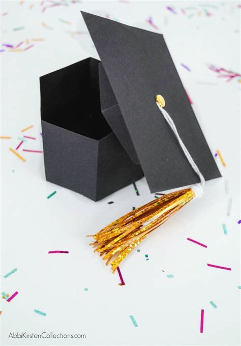 A Graduation Cap And Tassel On Top Of A Black Box With Confetti