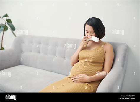 Pregnancy And Illness Sick Pregnant Woman Blowing Nose In Tissue Having Fever Sitting On Sofa