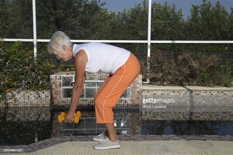 Senior Woman Bending Over And Lifting Weights High Res Stock Photo