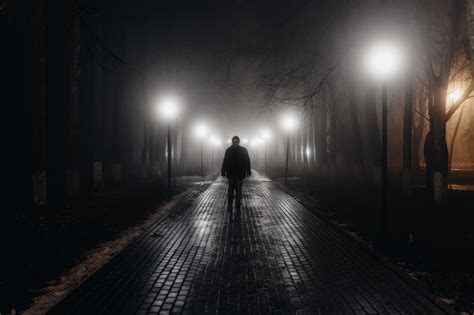 Sad Man Alone Walking Along The Alley In Night Foggy Park Front View