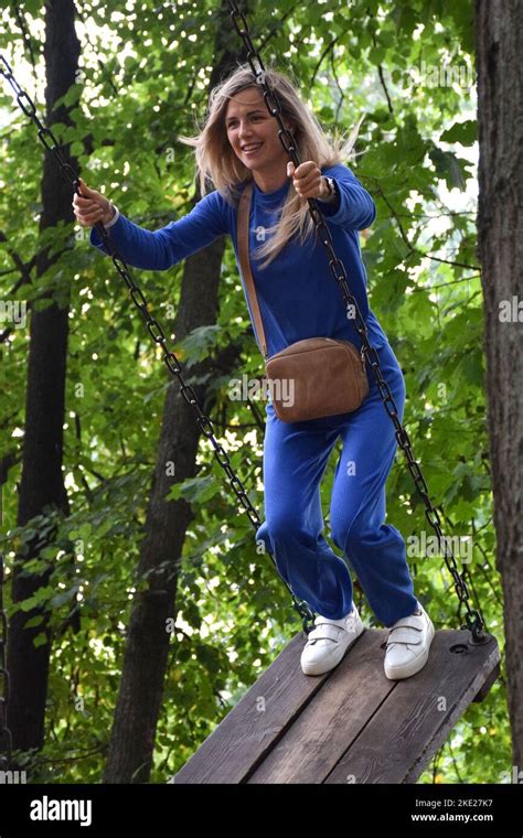 attractive blonde girl rides on a carousel swing in a blue suit with a handbag and smiles stock