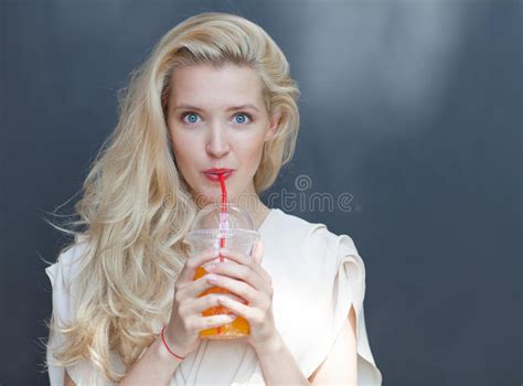 Красивая сексуальная блондинка с голубыми глазами выпивая напиток через