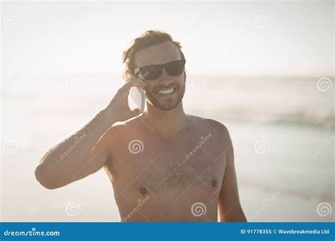Smiling Shirtless Man Talking On Mobile Phone At Beach Stock Image