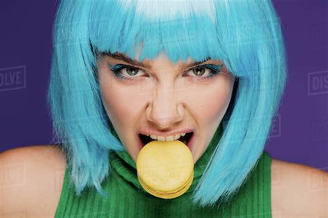 Aggressive Young Woman In Blue Wig Biting Macaron Isolated On Purple
