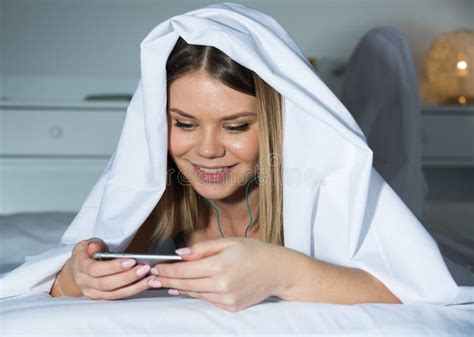 Young Woman Under Blanket On Bed With Mobile Phone Stock Photo Image