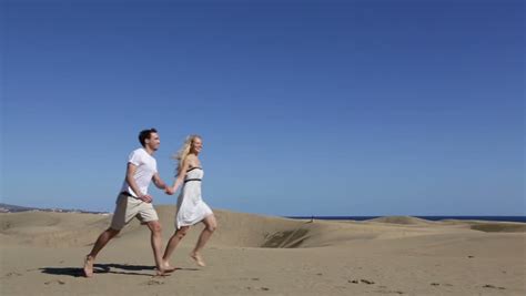 Mature Couple Holds Hands And Walk Over A Sand Dune And
