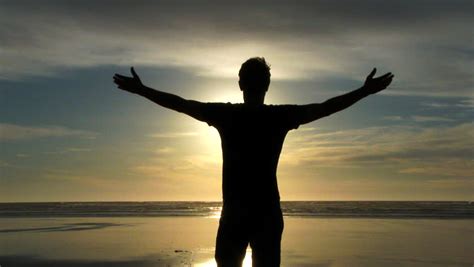 Silhouette Of Man Standing And Stretching Arms Up In Front Of Blue Sky