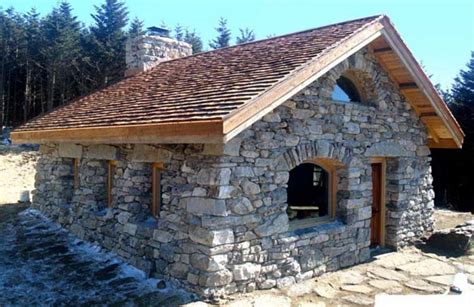 A Small Stone Building With A Roof Made Of Rocks And Wood On The