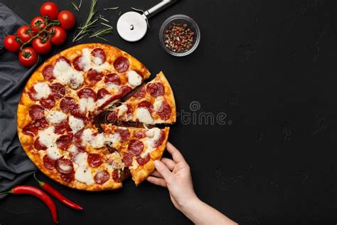 Woman Taking Slice Of Pepperoni Pizza On Black Table Stock Photo