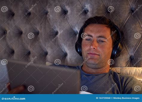 Man Wearing Wireless Headphones Lying In Bed Watching Digital Tablet